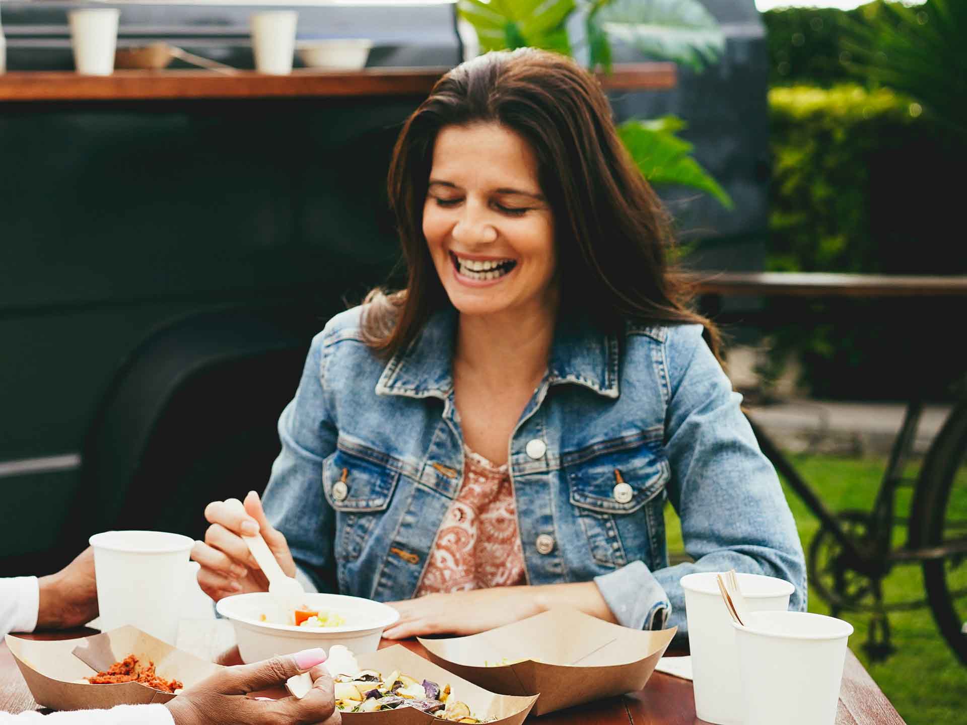 Woman smiling while enjoying a meal with friends, representing the everyday benefits of dental implants